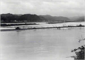 奈佐川左岸堤防の決壊カ所を大浜川左岸より望む
上流に見える橋は国道178号福田橋（豊岡市森津付近）